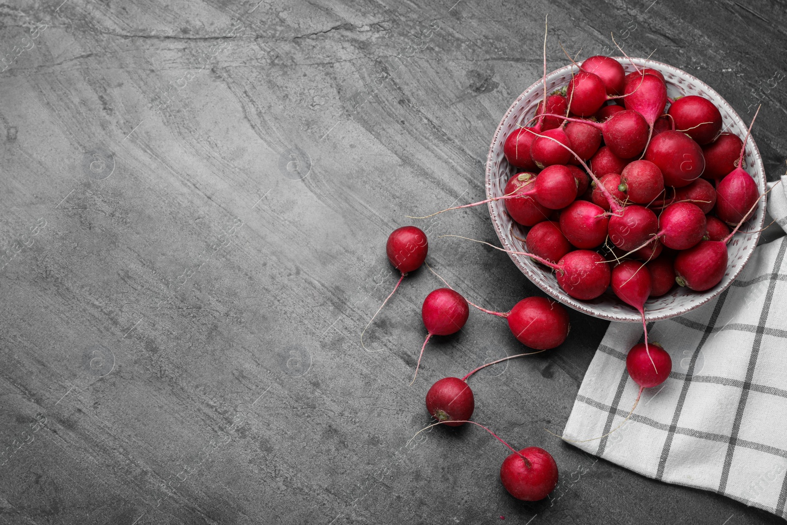 Photo of Bowl with fresh ripe radishes on grey table, flat lay. Space for text