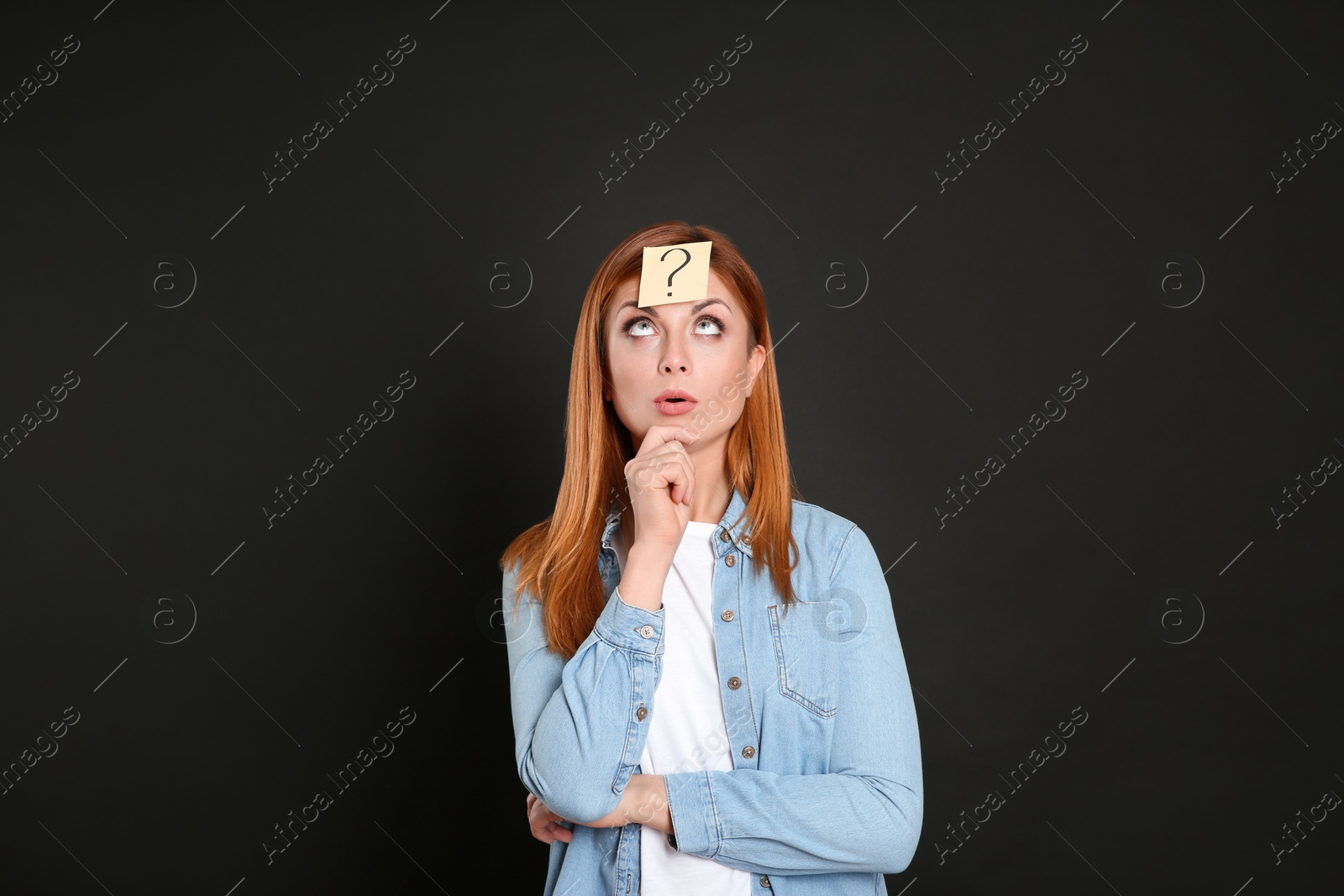 Photo of Pensive woman with question mark sticker on forehead against black background