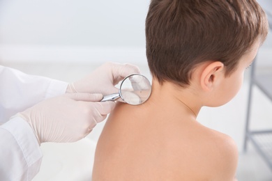 Photo of Dermatologist examining little boy's birthmark with magnifying glass in clinic