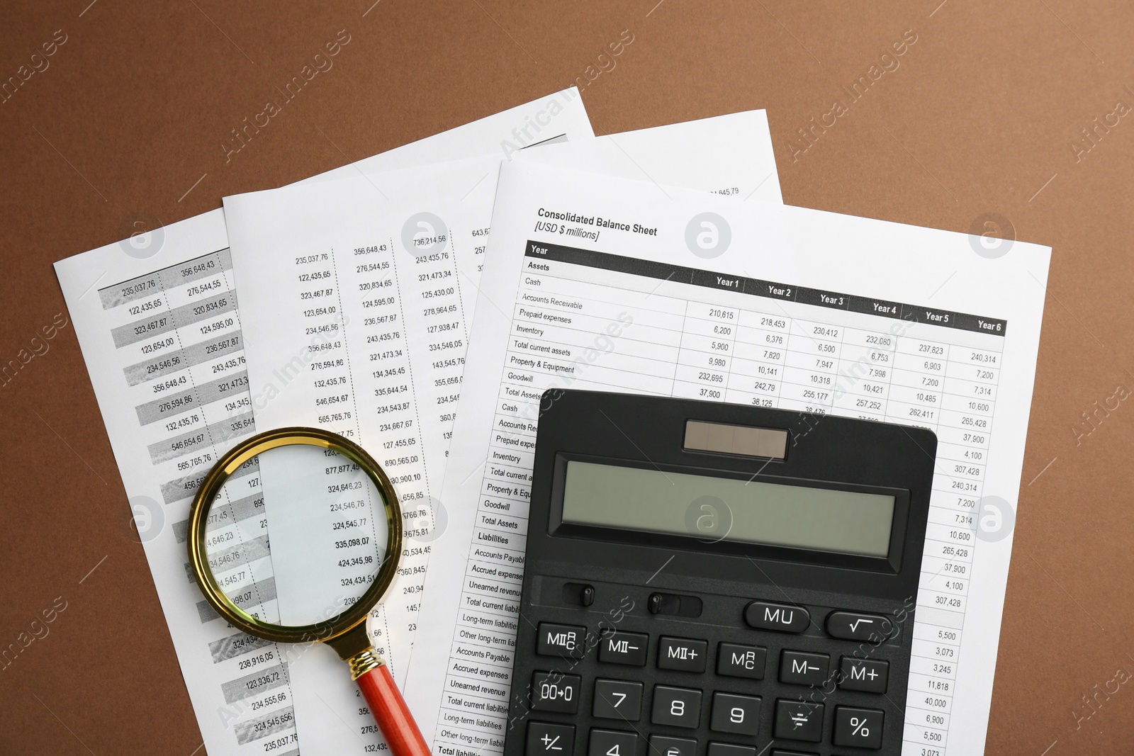 Photo of Accounting documents, magnifying glass and calculator on brown background, top view