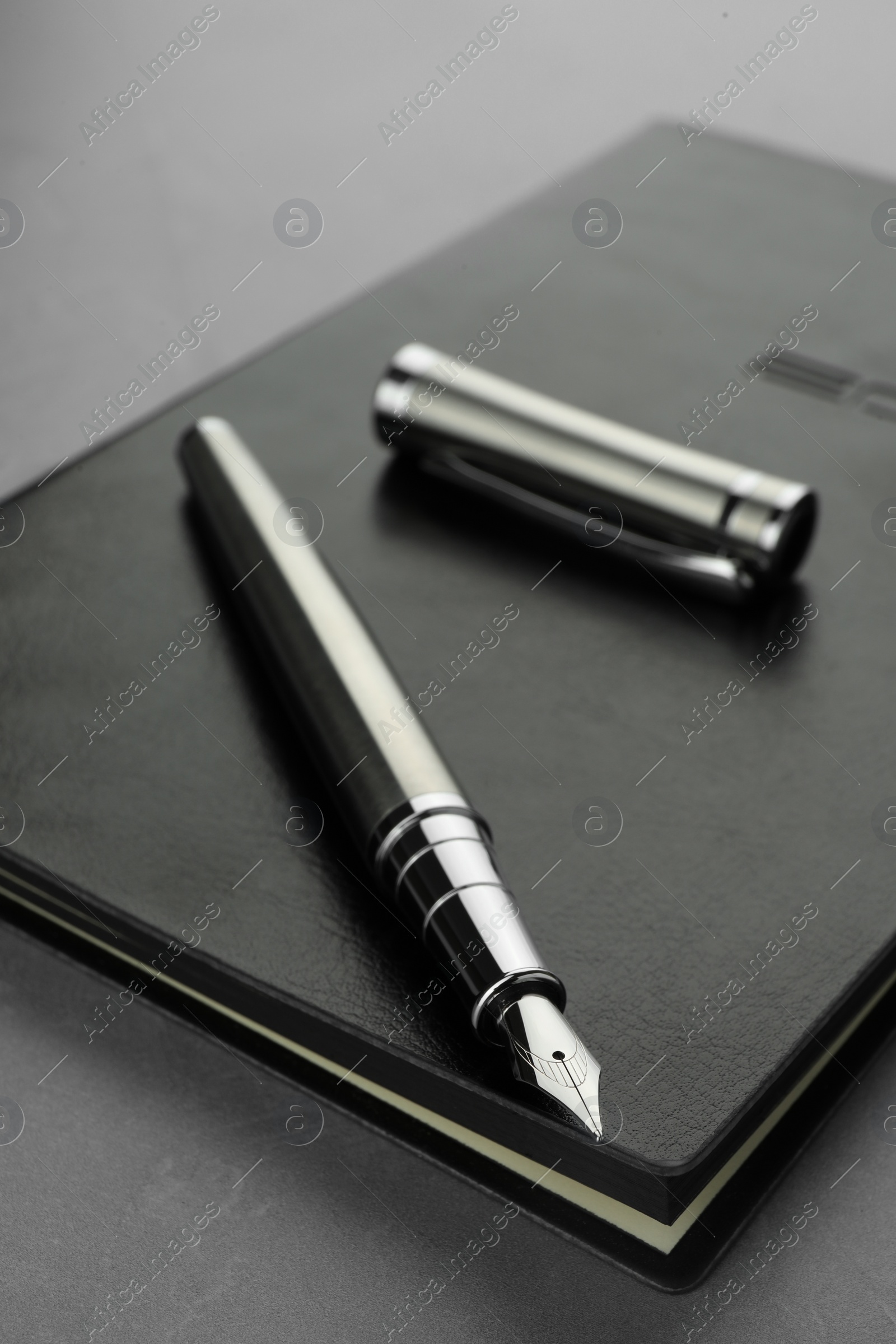 Photo of Stylish fountain pen, cap and leather notebook on light grey textured table, closeup