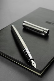 Stylish fountain pen, cap and leather notebook on light grey textured table, closeup