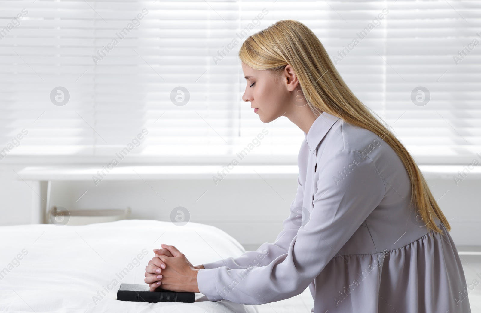 Photo of Religious young woman with Bible praying in bedroom. Space for text