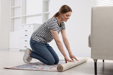 Smiling woman unrolling carpet with beautiful pattern on floor in room