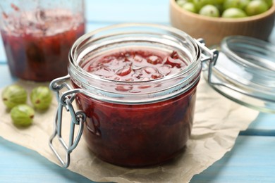 Photo of Jar of delicious gooseberry jam and fresh berries on blue wooden table, closeup