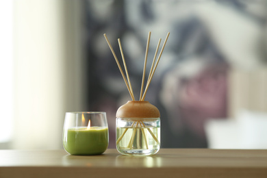 Aromatic reed air freshener and scented candle on table indoors