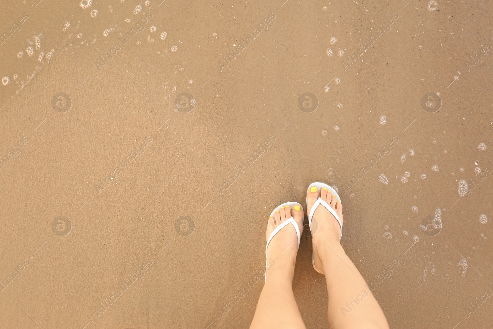 Photo of Top view of woman with white flip flops on sand near sea, space for text. Beach accessories