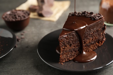 Photo of Pouring chocolate sauce onto delicious fresh cake on grey table, closeup