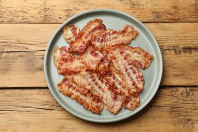 Photo of Delicious fried bacon slices on wooden table, top view