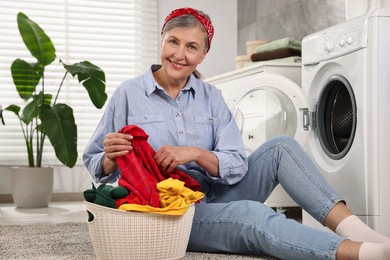 Happy housewife with laundry basket near washing machine at home