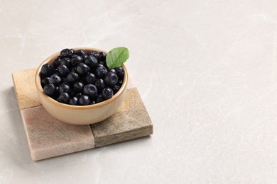 Photo of Bowl of tasty fresh bilberries on white table. Space for text