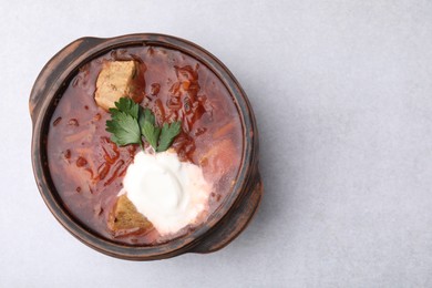 Photo of Tasty borscht with sour cream in bowl on light grey table, top view. Space for text