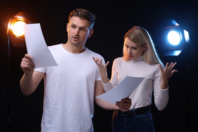 Photo of Casting call. Emotional woman and man with script performing on black background