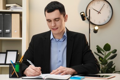 Photo of Man taking notes at table in office