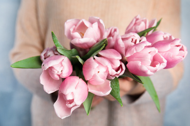 Woman with beautiful pink spring tulips on light blue background, closeup