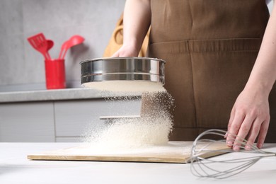 Photo of Woman sieving flour at table in kitchen, closeup