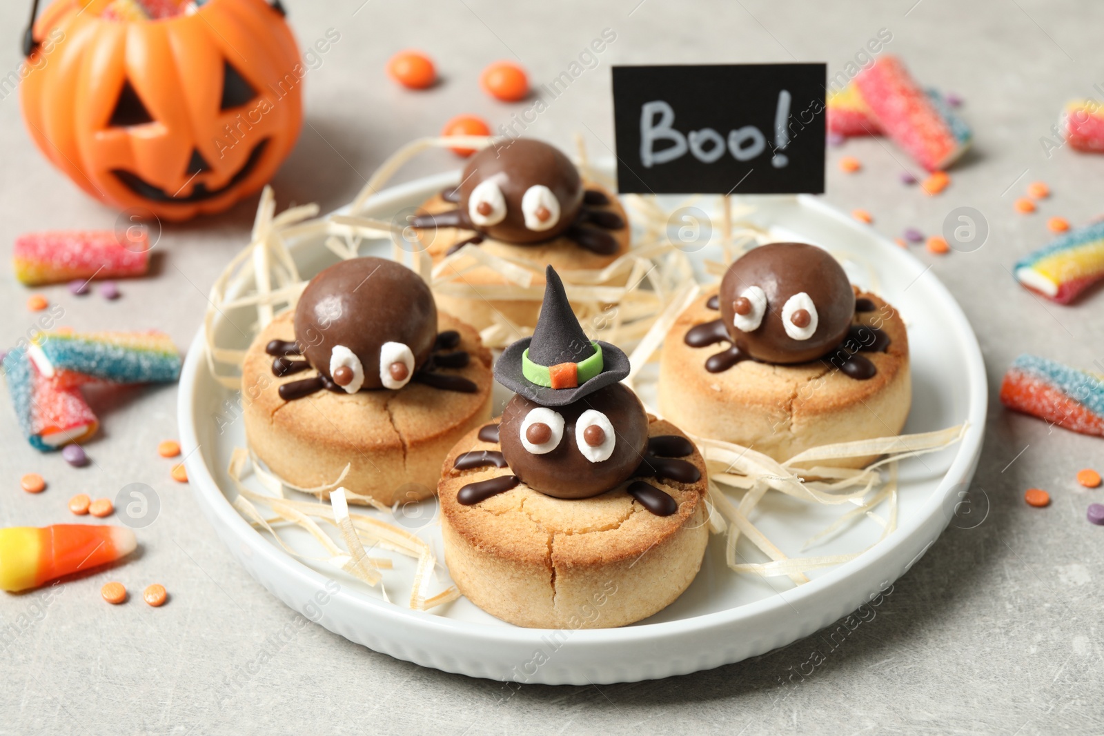 Photo of Delicious biscuits with chocolate spiders on light grey table, closeup. Halloween celebration