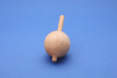 Photo of One wooden spinning top on blue background, closeup. Toy whirligig