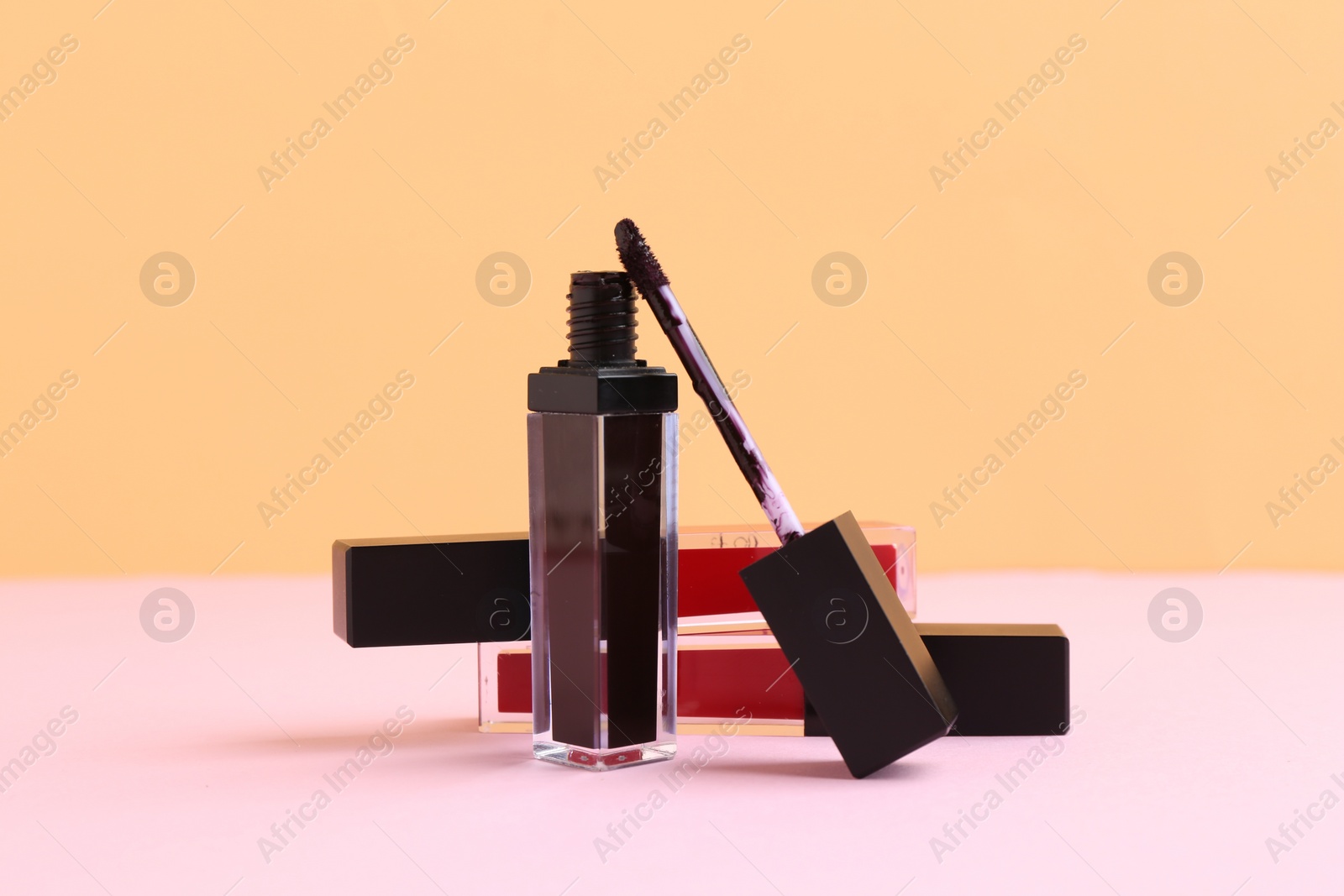 Photo of Different lip glosses and applicator on color background