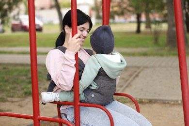 Photo of Mother holding her child in sling (baby carrier) on swing outdoors