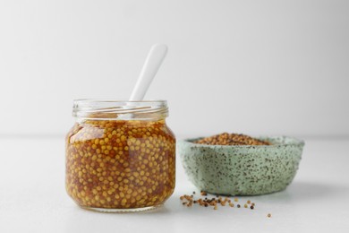 Whole grain mustard in jar and dry seeds on white table