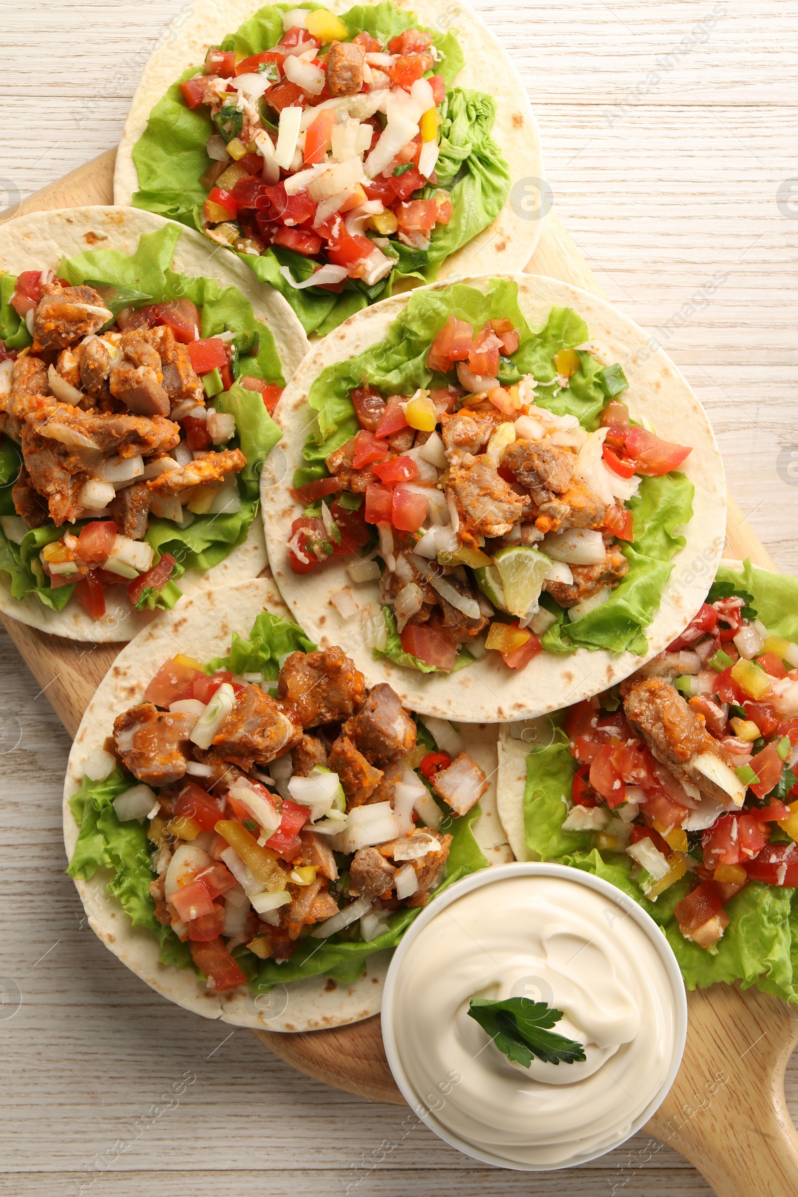 Photo of Delicious tacos with vegetables, meat and sauce on white wooden table, top view