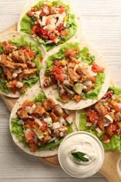 Delicious tacos with vegetables, meat and sauce on white wooden table, top view