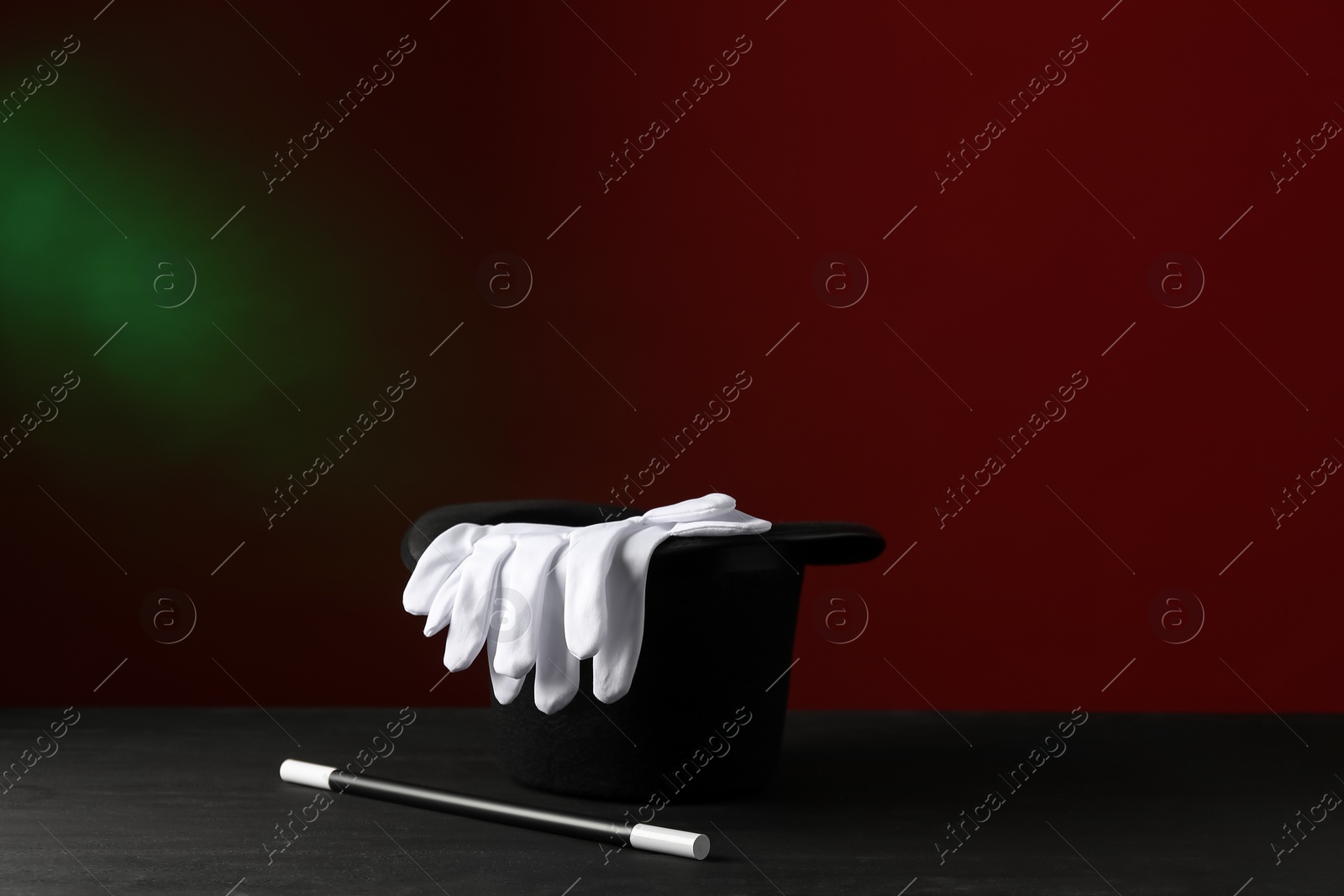 Photo of Magician's hat, wand and gloves on black wooden table against dark background