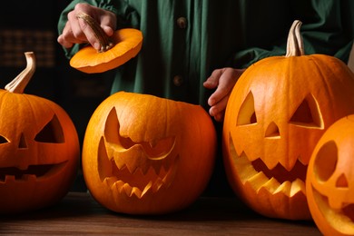 Photo of Woman with carved pumpkins for Halloween at wooden table, closeup