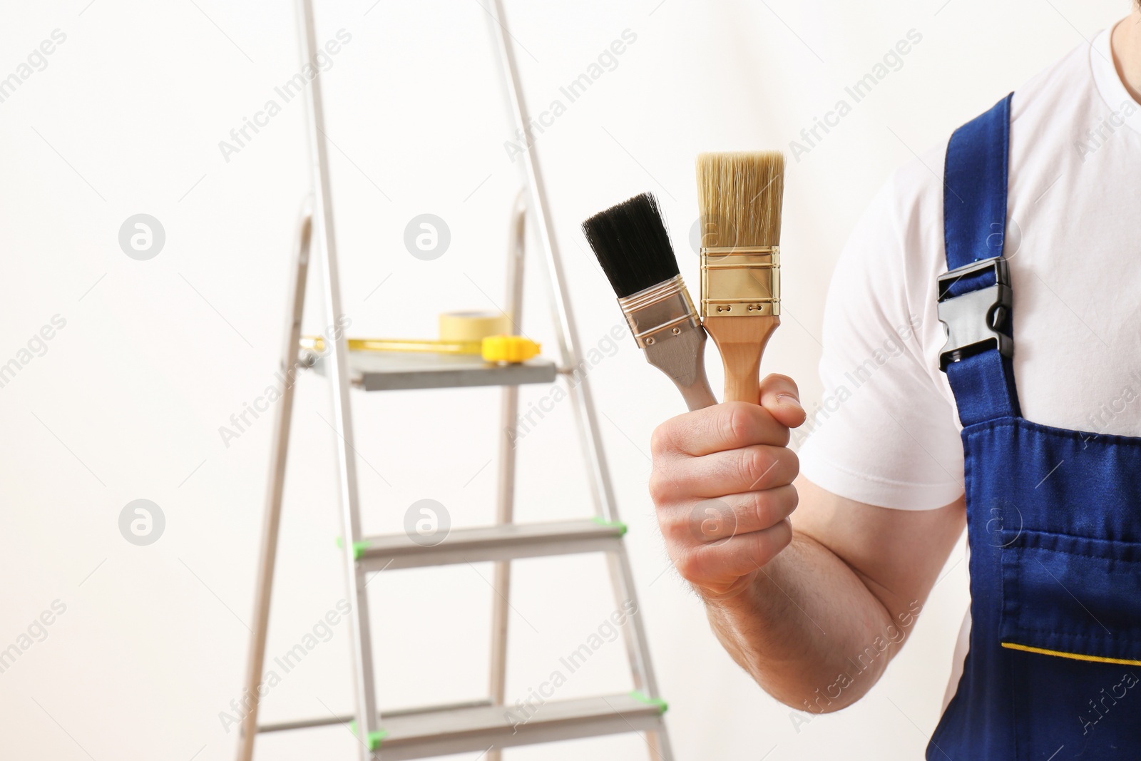 Photo of Male decorator with paint brushes in empty room, closeup. Space for text