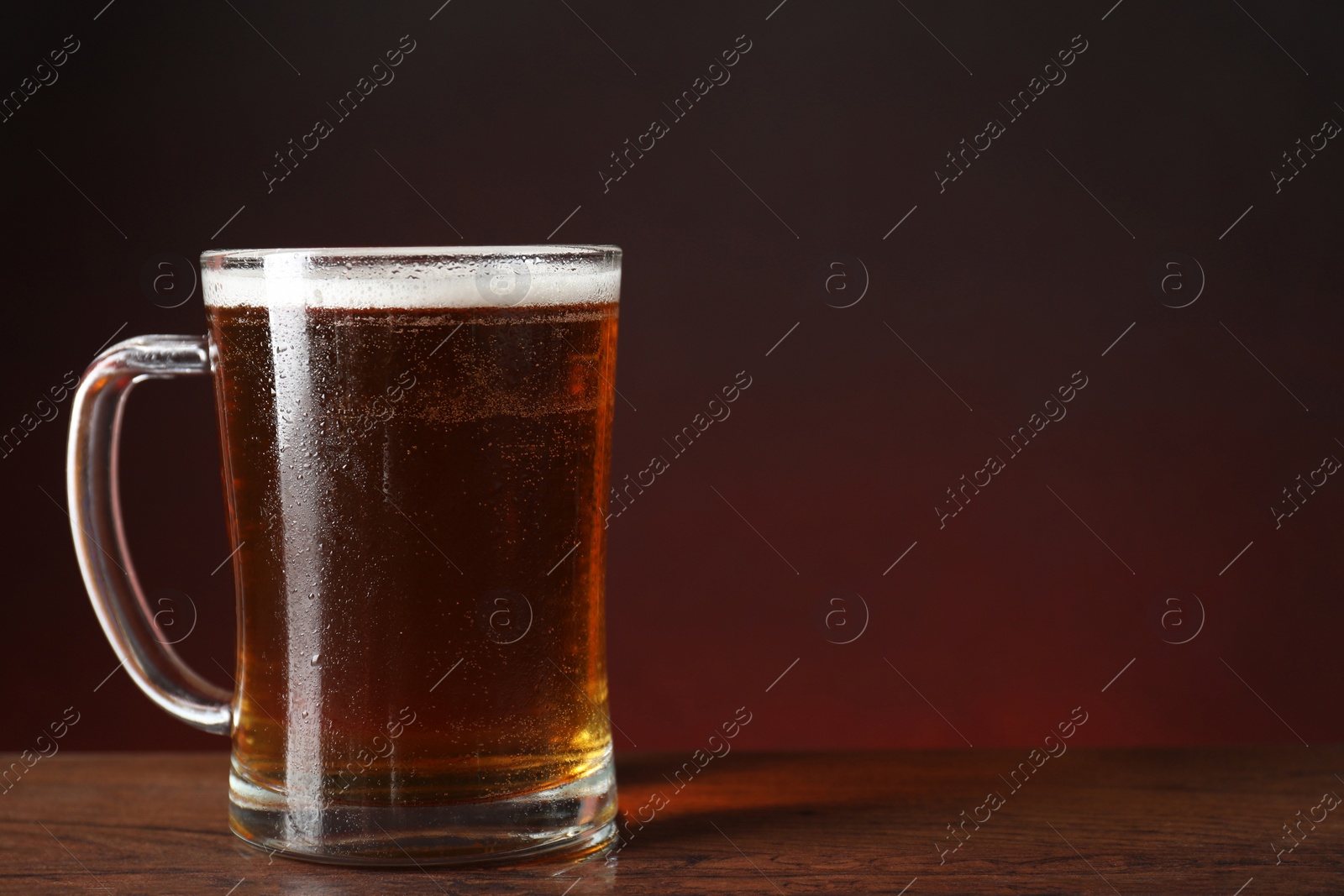 Photo of Mug with fresh beer on wooden table against color background. Space for text