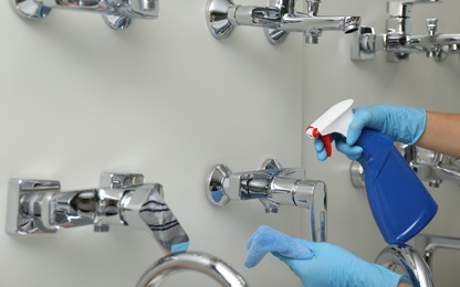Photo of Woman cleaning faucets with rag and detergent in bathroom fixtures store, closeup