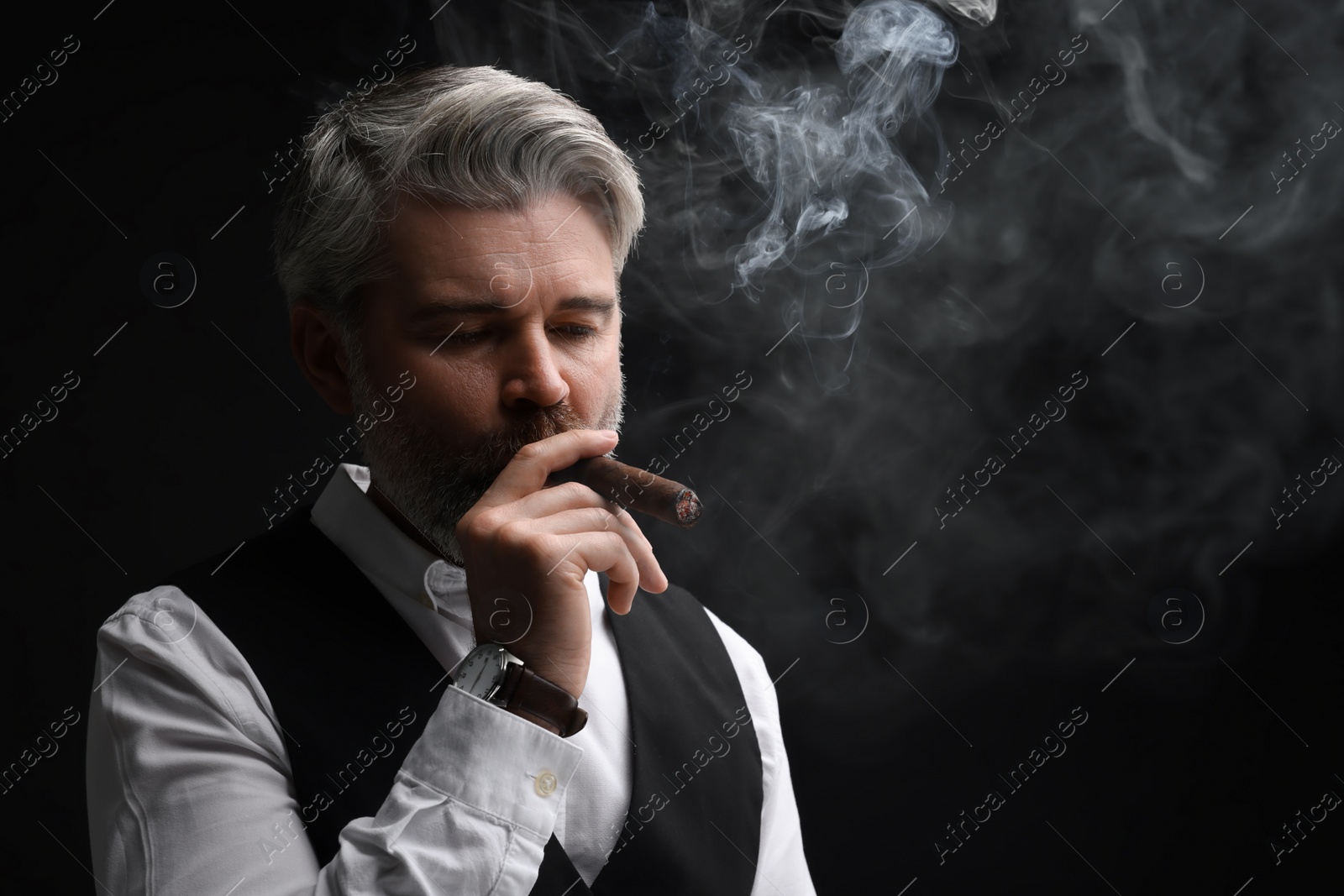 Photo of Bearded man smoking cigar against black background. Space for text