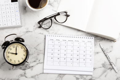 Flat lay composition with calendar and cup of coffee on white marble table