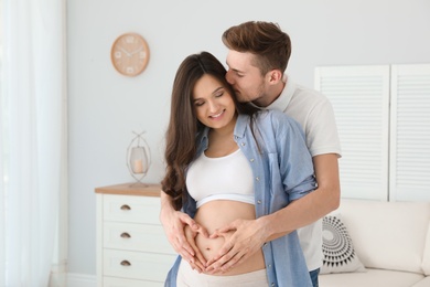 Photo of Pregnant woman and her husband showing heart with hands at home