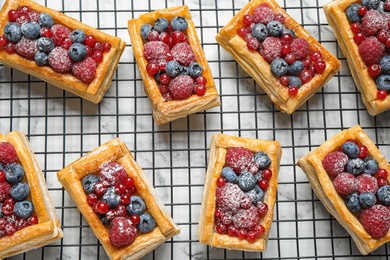 Cooling rack and fresh delicious puff pastry with sweet berries on white marble table, flat lay