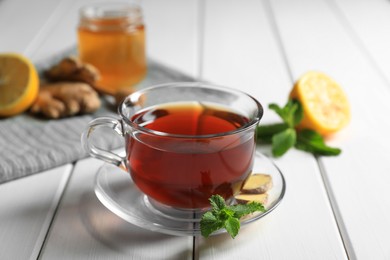 Photo of Cup of delicious ginger tea and ingredients on white wooden table, closeup