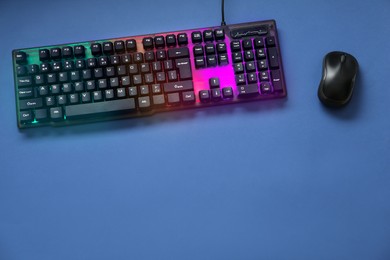 Photo of Modern RGB keyboard and mouse on blue background, flat lay. Space for text