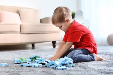 Photo of Cute little child playing with puzzles on floor indoors. Space for text