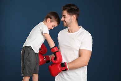 Dad and his son with boxing gloves on color background