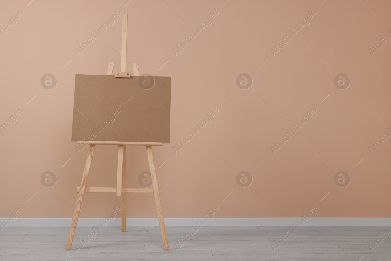 Photo of Wooden easel with blank board near beige wall indoors. Space for text