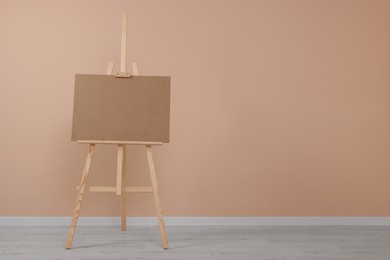 Photo of Wooden easel with blank board near beige wall indoors. Space for text