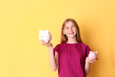Photo of Teen girl with piggy banks on color background. Space for text