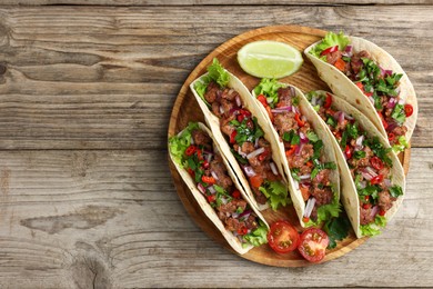 Delicious tacos with meat, vegetables and lime on wooden table, top view. Space for text