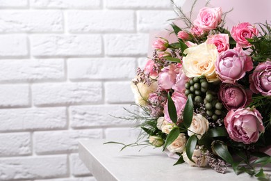 Beautiful bouquet with roses on light table near white brick wall. Space for text