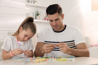 Photo of Happy father with his cute daughter making beaded jewelry at table in room