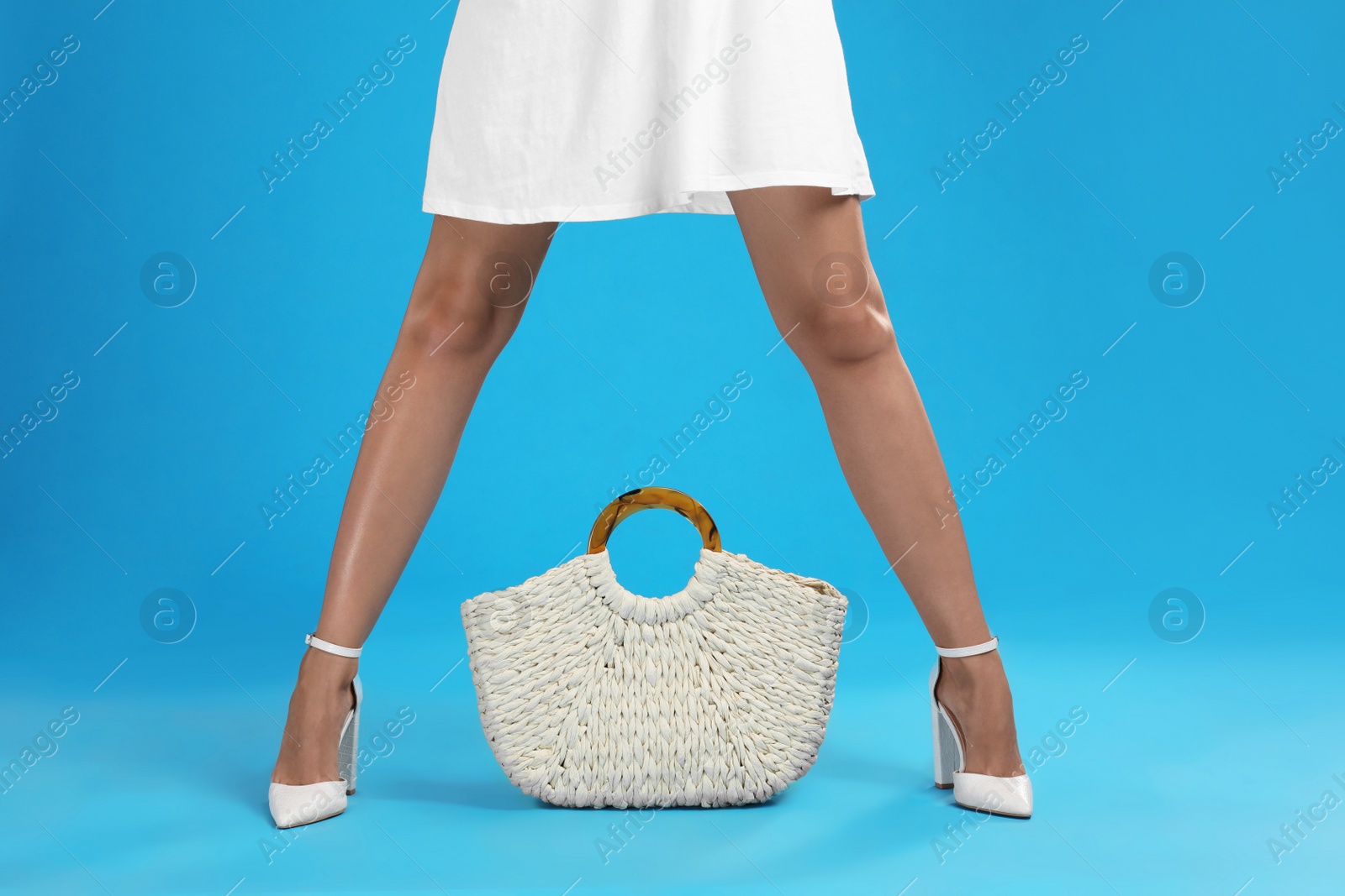 Photo of Young woman with stylish straw bag on light blue background, closeup