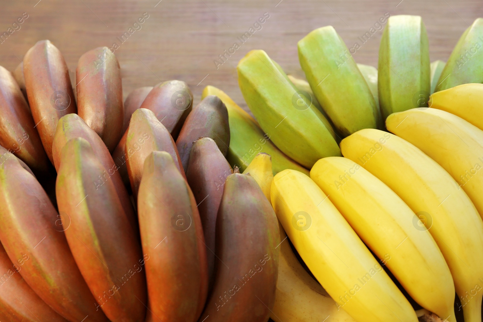 Photo of Different sorts of bananas on wooden table, closeup