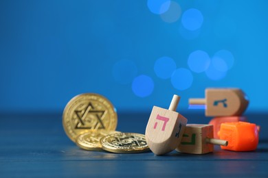 Photo of Hanukkah celebration. Dreidels with jewish letters and coins against blue background with blurred lights, closeup