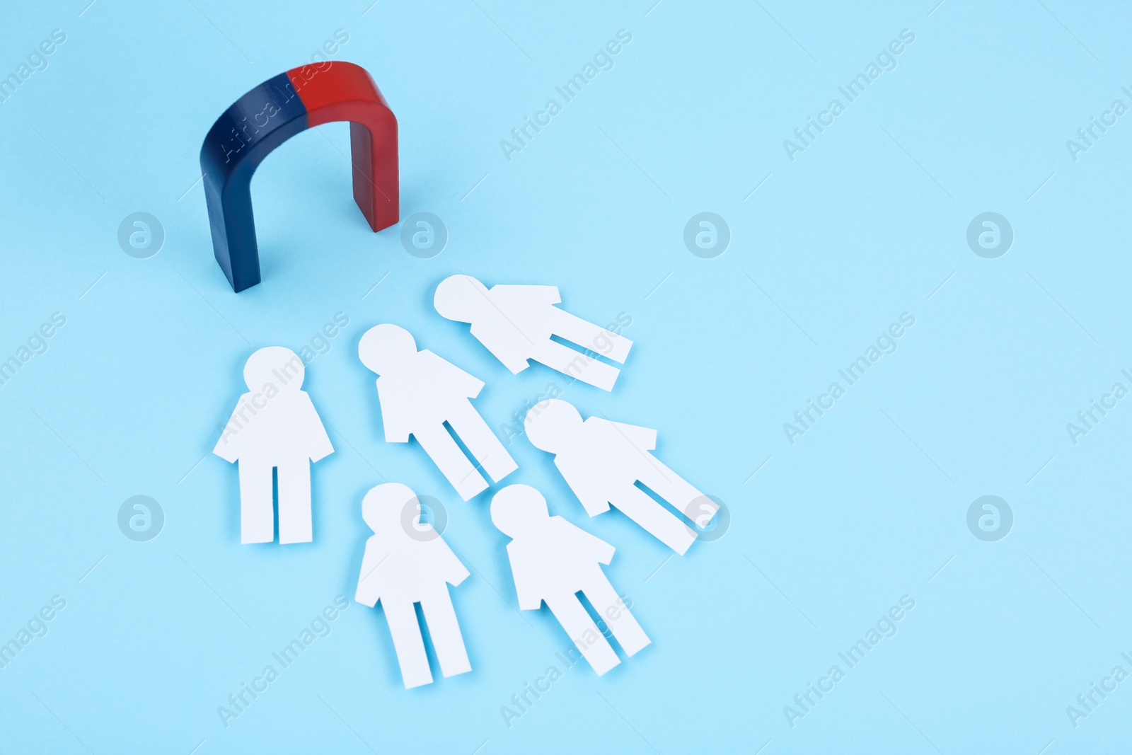 Photo of Magnet attracting paper people on light blue background